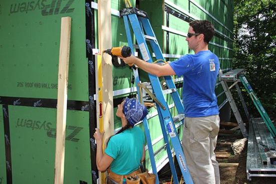 Project Managers Laura Boyle and Evan Smith plumb up and nail the first piece of shiplap board siding.