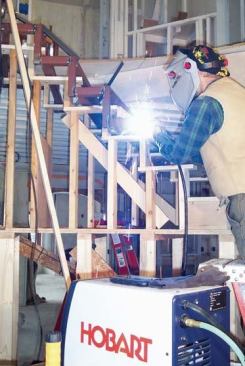 Once the frame is in the correct position, he connects it to the preceding tread frame by welding it to a vertical riser bar.
