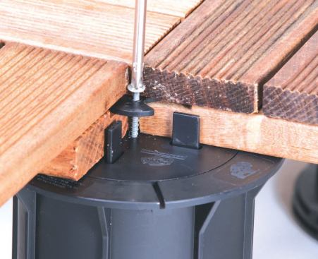 A plastic disk and a single screw secure the corners of four ipe tiles at every pedestal. Spacer tabs maintain a uniform 1/4-inch gap between adjacent tiles; a wedge-shaped cutout in the disk can be rotated to allow a tile to be removed.