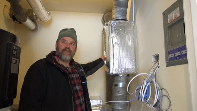 Steve Davis in the mechanical room of the modular dwelling. A three-component system incorporating three different heat pumps serves the unit's needs: There's a Mitsubishi mini-split for primary heating and cooling, a heat-pump water heater, and a heat-pump-boosted Conditioning Energy Recovery Ventilator (CERV) that maintains air quality and distributes heat and fresh air to distant rooms.