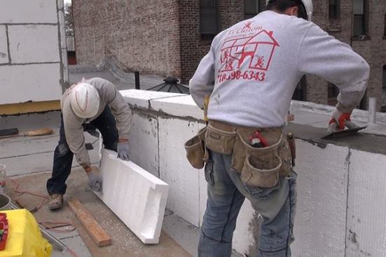 A carpenter from J’s Custom Contracting uses the toothed edge of a mortar trowel to scratch grooves into the underside of a piece of 4-inch EPS foam, to improve adhesion of the cementitious mortar used to attach the foam to the masonry parapet wall as part of a continuous insulation and finish system for the building’s masonry bearing wall and parapet wall. The foam insulation on the parapet wall will tie into the polyurethane insulation on the building’s roof deck, providing a continuous thermal control layer that keeps the building’s wall and roof structural mass within the insulated plane of the building.