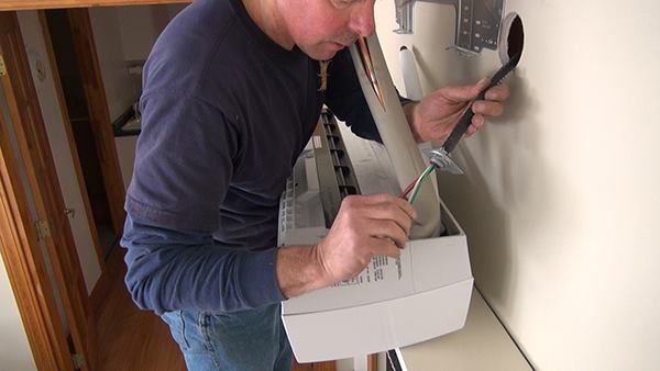 Chris Blaisdell prepares to connect the system’s color-coded electrical power and control wires to the wall-mounted fan for the indoor unit of the heat pump.