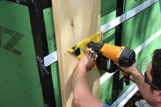 Evan Smith nails siding to the wall using an inexpensive site-made nail placement jig: a plastic Speed Square drilled out to accept the rubber nose of a Bostitch coil nailer.