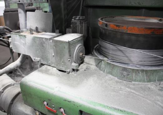 This is the first of many dies and drums inside of the wire drawing machine in the previous photo. The wire enters from the left and passes through an open box containing chips of a soap-like substance that lubricates the surface before it enters the die. The die is inside the green box. After exiting the die the wire is coiled on a drum and then sent through a series of smaller and smaller dies—each with its own drum and box of lubricant.