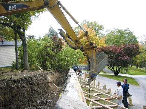 A heavy wood block strapped to the excavator's bucket distributed the pressure across a 4-foot section of shoring as the wall was eased upward. Though relatively little lifting force was needed, only a large machine could supply the necessary reach across the excavation.