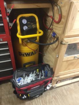 An air compressor is installed below a cabinet on the right side of the trailer. The flexible line contains a water filter, and connects to a copper line that runs to the back of the trailer.