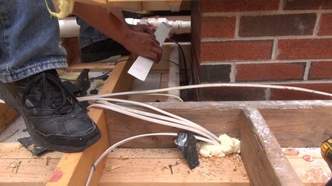 Working by feel as much as by sight, Phillips eases a strip of metal flashing into place between the chimney and the framing.