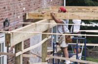 Carpenters set the joists for a freestanding deck; the band will remain spaced away from the brick veneer wall.
