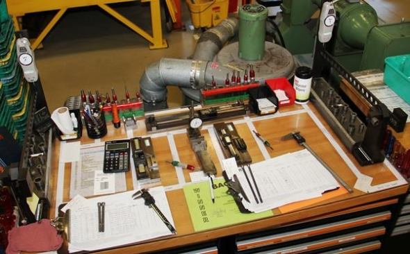This work table is on the factory floor. The drawers below contain various small parts for the machines. The calibration and measuring equipment on top are for setting them up and verifying they are producing to the correct specification.