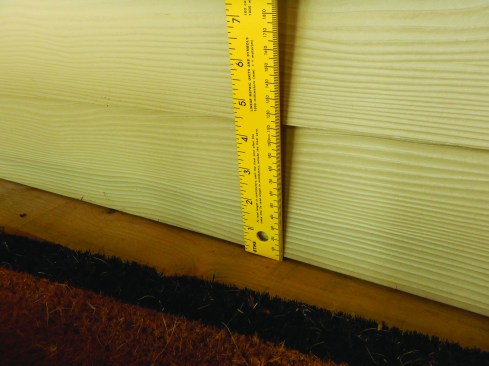 Per the manufacturer's installation instructions and the Evaluation Services Report (which take precedence over prescriptive buildin codes), there should  be at least 1 inch to 2 inches of clearance between the siding boards and the porch surface.