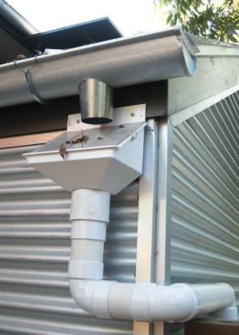 Rain heads are installed in the downspouts. The sloped screen of the rain head diverts debris into the yard while allowing water to pass through. A second, finer screen underneath prevents mosquitoes and other insects from getting into the tank.