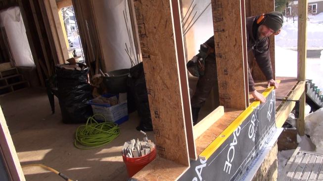 Muennich uses a 6-foot level to check the alignment of three side-by-side window bucks as the crew builds out the wall.