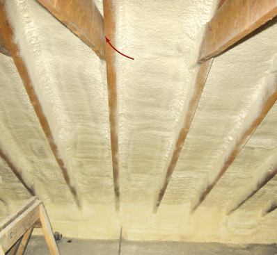 This correctly applied closed-cell foam has been sprayed directly against the underside of the roof deck. To eliminate air leaks at the eaves, the foam has been extended beyond the top plate to form a seal against the attic floor. One minor omission: An additional shot of foam to each of the cracks between rafters and collar ties (arrow) would have prevented any possible air movement through that interface.