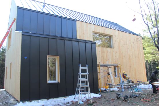 On the north side of the Blue Hill house, dark metal roofing wraps down part of the wall.