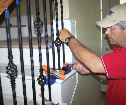 To keep the balusters from sliding back down into the tread holes, I fix each one in place with a spring clamp while the epoxy sets up.