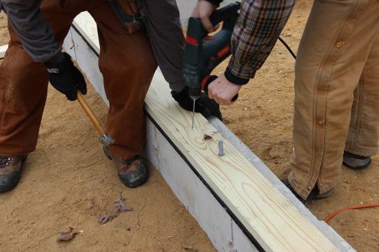 Mike Hill holds the sill plate in position while carpenter Russ Laffin drills a pilot hole for a hand-driven split shank fastener.