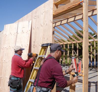 To air-seal the 1/2-inch sheathing to the framing as it was installed, one carpenter laid beads of foam on the framing edges while another followed with a nail gun.