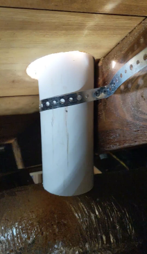 Once the fan is installed, the author strategically cuts a hole as close to a framing member as possible. This member will provide support for the vent pipe. Temporarily using pipe strap, he attaches a short length of 3-inch PVC pipe to the rafter next to the hole.