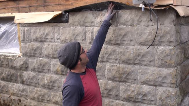 Thompson Johnson Woodworks lead carpenter Mark Pollard explains the re-worked sill detail for the house. The sill beam, which was found to be suffering from rot in a few limited areas, was jacked up and shimmed straight (if not level). The crew has isolated the sill beam from the block foundation with Grace membrane.