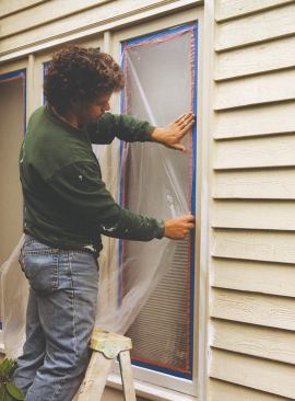 He lays painter's plastic onto the tape, trimming it to size with a razor blade.