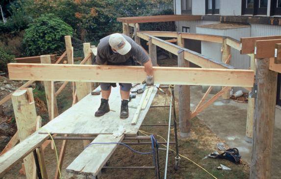 The author treats the wood with a borate preservative before placing the beams in their pockets. Note the torch-down roofing membrane applied to the beam and post tops in the background.