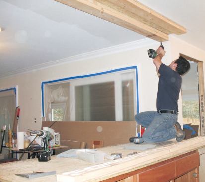To anchor the hanging peninsula cabinet, a crewmember fastens double 2x6 cleats to the ceiling framing with structural screws and glue.