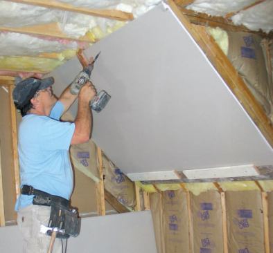 The cleat supports the lower edge of the drywall, allowing him to align the sheet with one hand while driving screws into the framing with the other.
