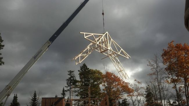 A crane flies a set of roof trusses into place for the Surry Passive House. Achieving the necessary R-values will require packing the cathedral truss voids full of cellulose insulation.
