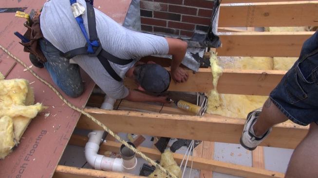Weatherization tech Scott Pillips air-seals a framing joint with gun foam before starting to install air-sealed metal flashing over the gap between the brick chimney and the wood-framed chimney chase.