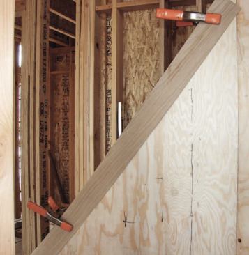 By using adhesive and staples and lots of pressure, we got the plywood to conform to the arc. I ran it long at the top, then clamped on a strip of 1/8-inch oak for scribing a fair curve about 4 inches above the tread nosings.