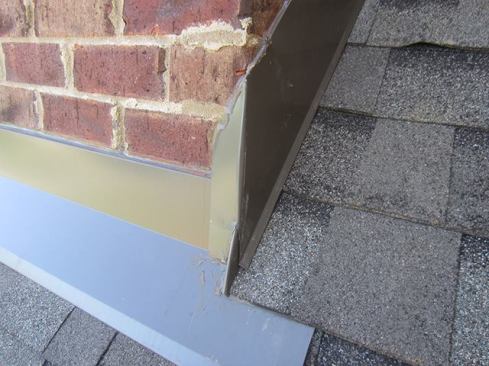 A similar meager attempt was made to flash this chimney. The apron and sidewall flashings were kerf-cut in about 1/2 inch and held in place with nails and caulk—a bad idea. The chimney’s apron should be composed of a two-piece flashing with a through-wall counterflashing lapping over a separate apron flashing. The main point of installing two-piece through-wall apron and sidewall flashing is so you have the ability to remove apron, or "skirt", thereby having access to the step flashing when you reroof. This chimney is currently being taken down to roof level, and the new copper pan flashing will be installed in stair-step fashion.