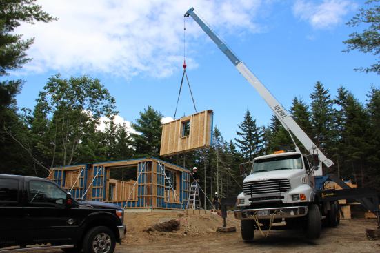 A crane swings a superinsulated wall panel into place on the insulated slab foundation in Blue HIll, Maine. Previously set panels have already been plumbed and braced.