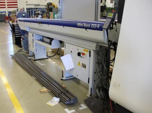 The metal rods on the floor will be loaded into the hopper above (the part that says Mini Boss) and fed into the CNC machine on the far right side of the shot – to be machined into a conduit reamer that can be used in a drill or impact driver.