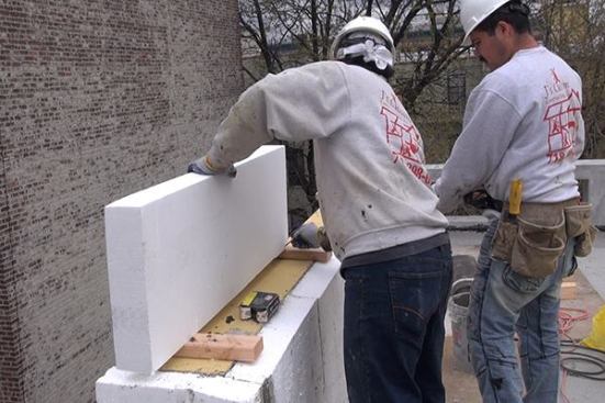Foam is measured and marked in place before cutting and installing it onto the masonry parapet wall.