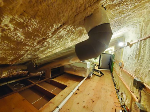 In the attic above the mudroom and gym, the author created a 1-inch air gap below the roof sheathing with 1-inch extruded polystyrene foam between the rafters, then applied 7 inches of closed-cell spray foam, for a combined R-value of around R-55. The stray foam was carried down the walls to create a cohesive insulation barrier.