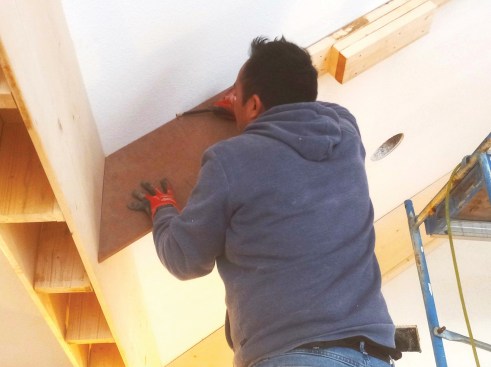Workers use templates to confirm angles at both the top and bottom of the beam. They also transfer a mark from the template to the ceiling so that measuring the length of the panel is easier.