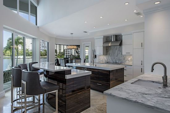 Custom islands made of ebony with a high gloss lacquer finish and topped with pompei quartz are the focal point of this kitchen remodel that is freshly balanced with white cabinetry and marble granite.
