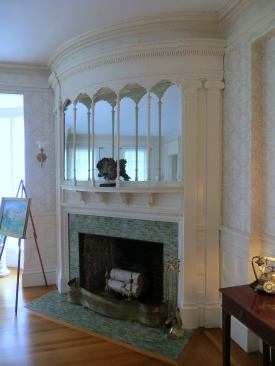 This curved fireplace with a mirrored overmantle was inspired by the Palace at Versailles. Note the Ionic columns that support the curved tablature while narrow columns and arches in front of the mirror reflect the columns and arches of the porch outside.