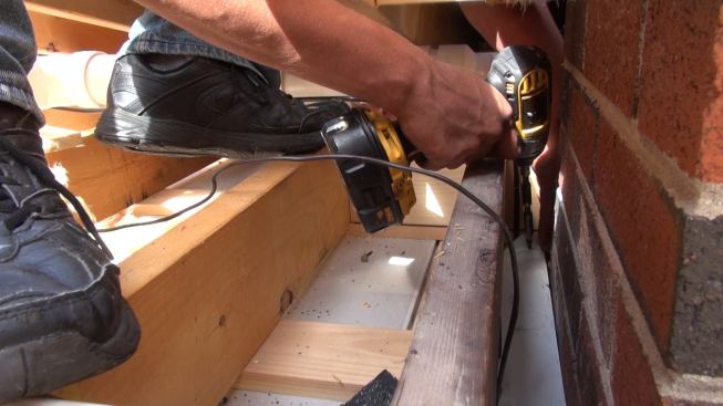 Phillips screws the metal flashing down onto the chimney chase framing.