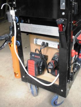 I further customized the cart by installing vertical dividers in the lower shelf and attaching a charging station to the side of one. Here you can see the chargers for 18- and 12-volt batteries. This location also contains a phone charger. The cart contains a power strip that can be plugged in on site or in the back of the truck.