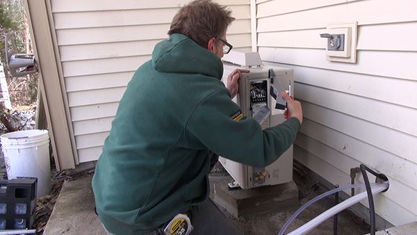 Outside, Dave Ragsdale removes a protective housing from the outdoor unit of the mini-split system to gain access to the wiring connections for the system.