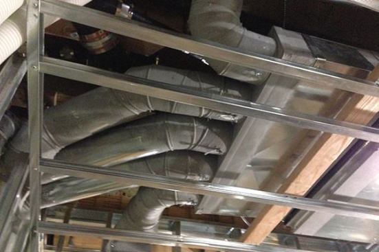 Supply ductwork from a 9,000-Btu/hr air handler, one of two for the home, leads out of the unit and into roof and wall chases. The ducts will feed distant rooms in the house, enabling the system to mix air volumes in the building, equalize temperatures, and distribute passive solar heat and other internal gains in the building around the various occupied spaces. The galvanized ductwork is sealed with mastic for airtightness. Light-gauge steel framing for the bathroom ceiling will be covered with drywall soon.