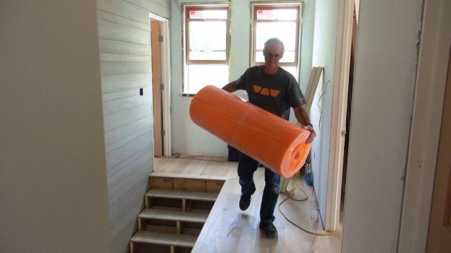 Tile contractor Tom Boucher carries a roll of Schluter Ditra polyethylene floor underlayment to the work area. Easy to carry and store, the roll has more than enough material for the master bath floor.