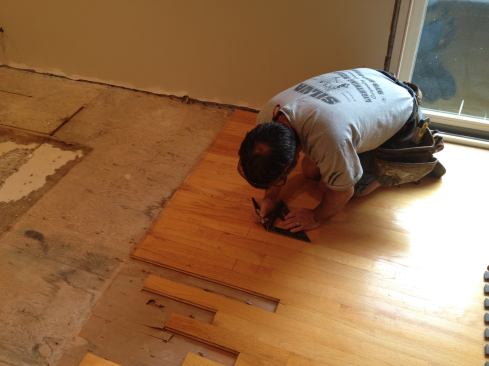 The original flooring ended in a straight line where the sheet flooring in the old kitchen began. Here Manny draws square lines across the boards so that they end in a random pattern to disguise the transition. An X on each board marks the section to be removed.