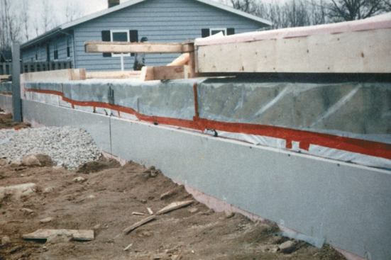 The band joist is wrapped with Tenoarm, a very tough, transparent polyethylene. The Tenoarm has been taped to the white polyethylene stapled to the bottom of the mudsill, and then wrapped up onto the subfloor.
