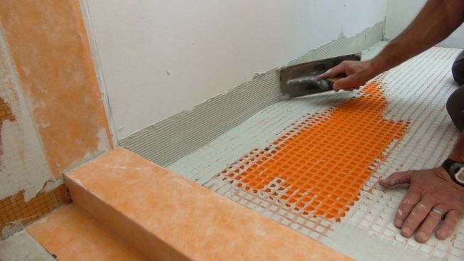 Boucher applies a measured mortar bed to the drywall using a Kerdi trowel with one-eighth-inch notches.