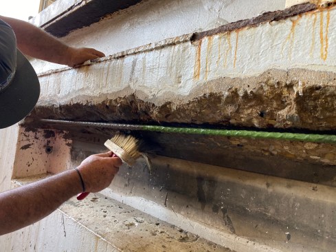 After wetting down the concrete, a crew member brushed on a slurry mix, working it into the rough surface of the concrete and rebar with a mason’s brush.
