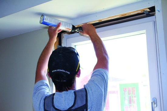 Working steadily, he pulls a bead across the window head. Note that jamb extensions have not yet been installed.