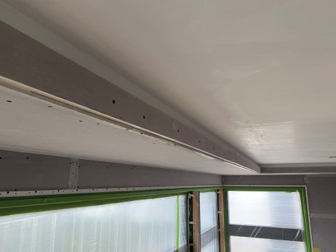 The bottom corner of the ceiling and the 2x4 are covered with plasterboard.