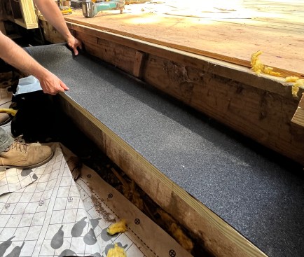 Reframing the floor began with rebuilding the sill where it connected to the deck. After digging out the rotted framing, the crew installed an ice-barrier membrane on a new rim joist.  (Here the rim joist is on its side, prior to installation, so the ice-barrier can be applied.)  